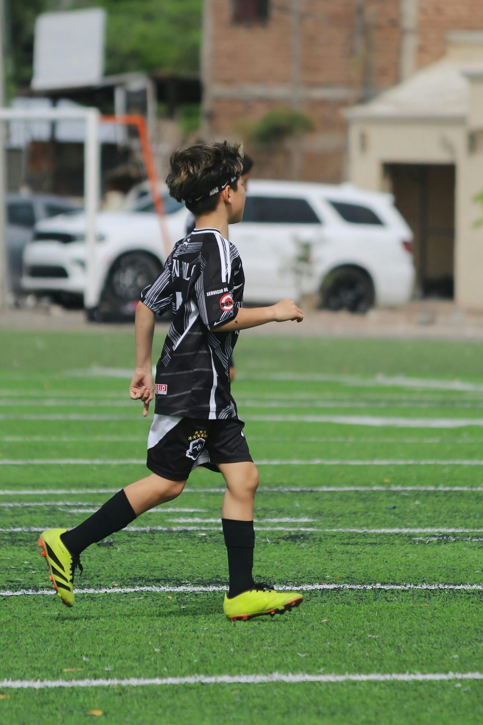 Young boy playing soccer on outdoor turf field, wearing team uniform.